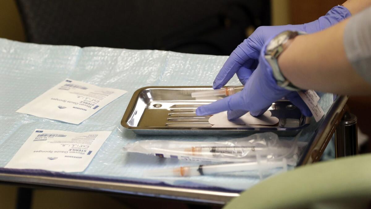 A healthcare worker prepares syringes, including a vaccine for measles, mumps, and rubella, for a child's inoculations at International Community Health Services in Seattle.