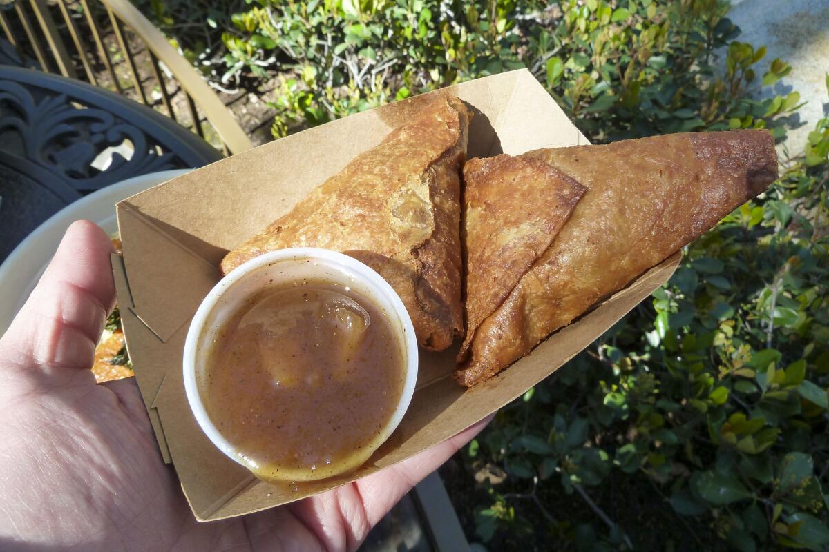 Potato sambusas in a cardboard tray with a plastic cup of sauce