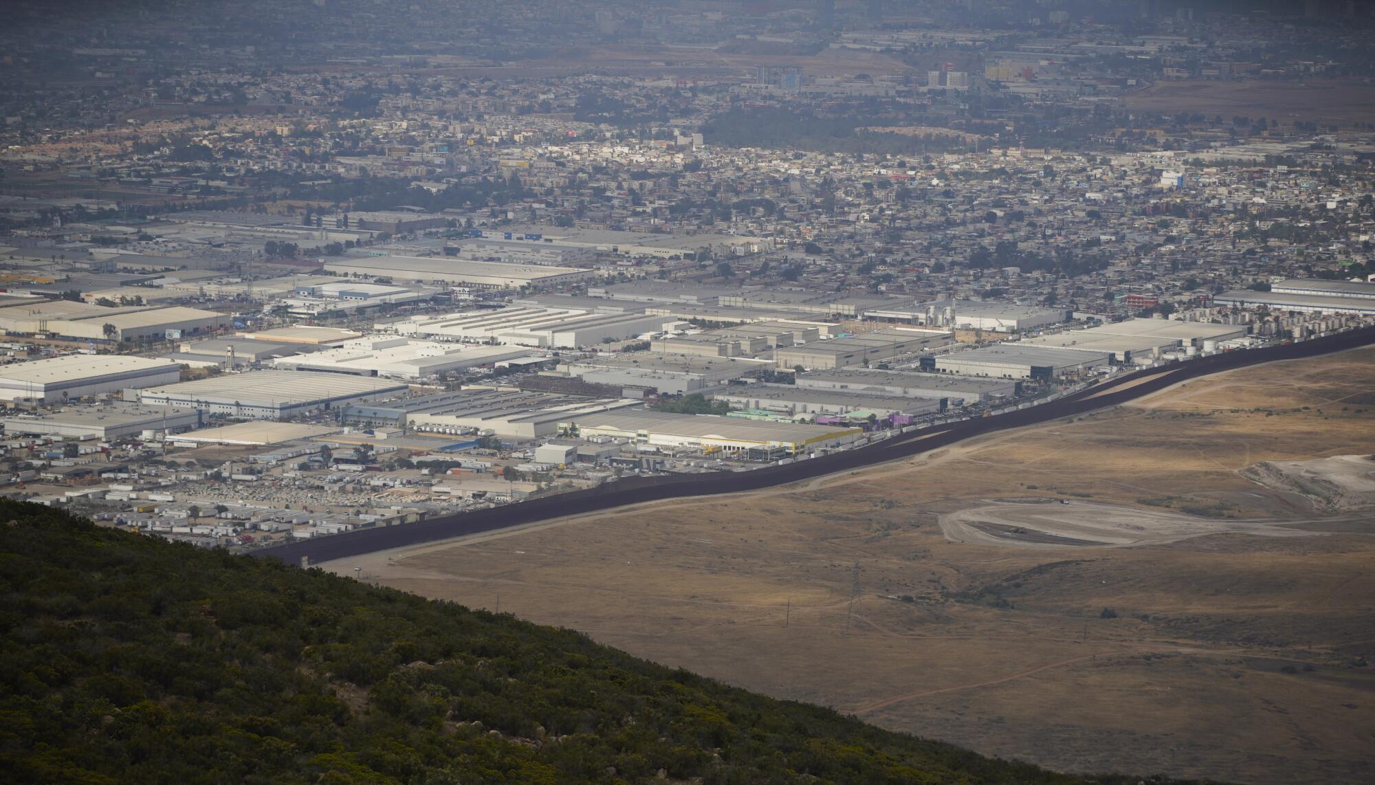 Many buildings are on one side of the border fence and open land is on the other side. 