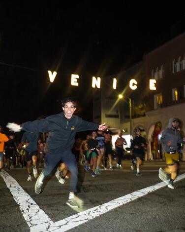 Runners at night under an illuminated sign that says Venice