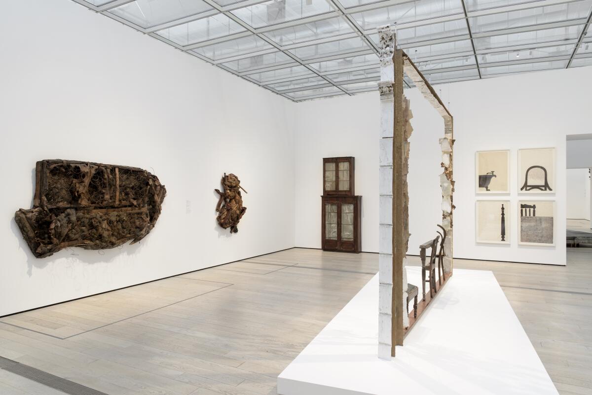 A view of white walled galleries show objects made from wood and other found domestic materials on a plinth and on a wall