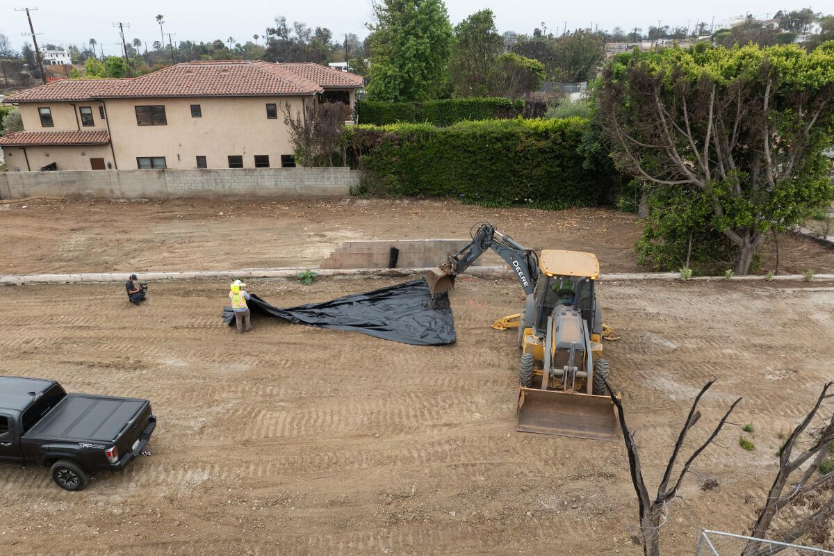 workers spread a tarp on a bare field with a backhoe and a truck