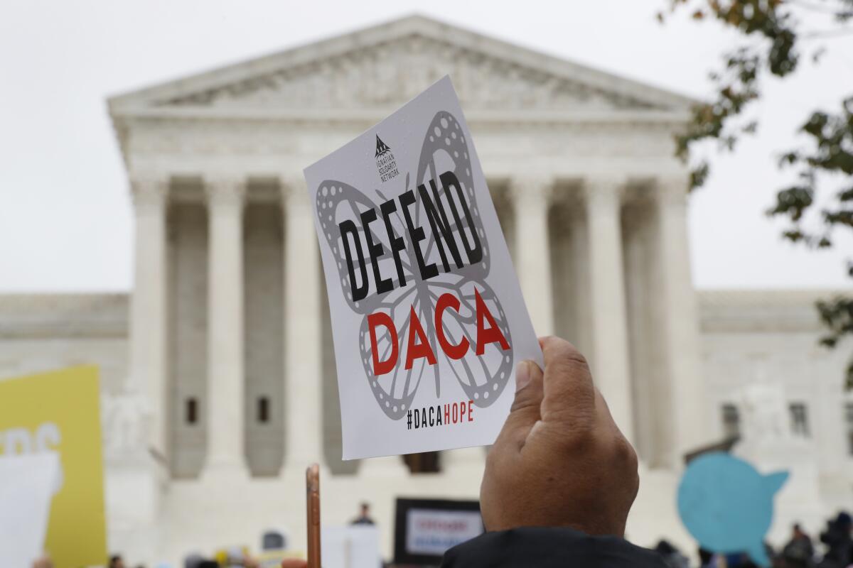 A hand holds up a sign saying "Defend DACA" in front of the Supreme Court building. 