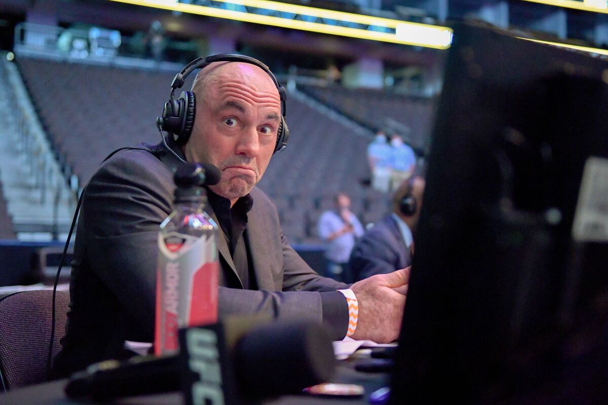 Joe Rogan, wearing headphones, raises his eyebrows as he faces a camera.
