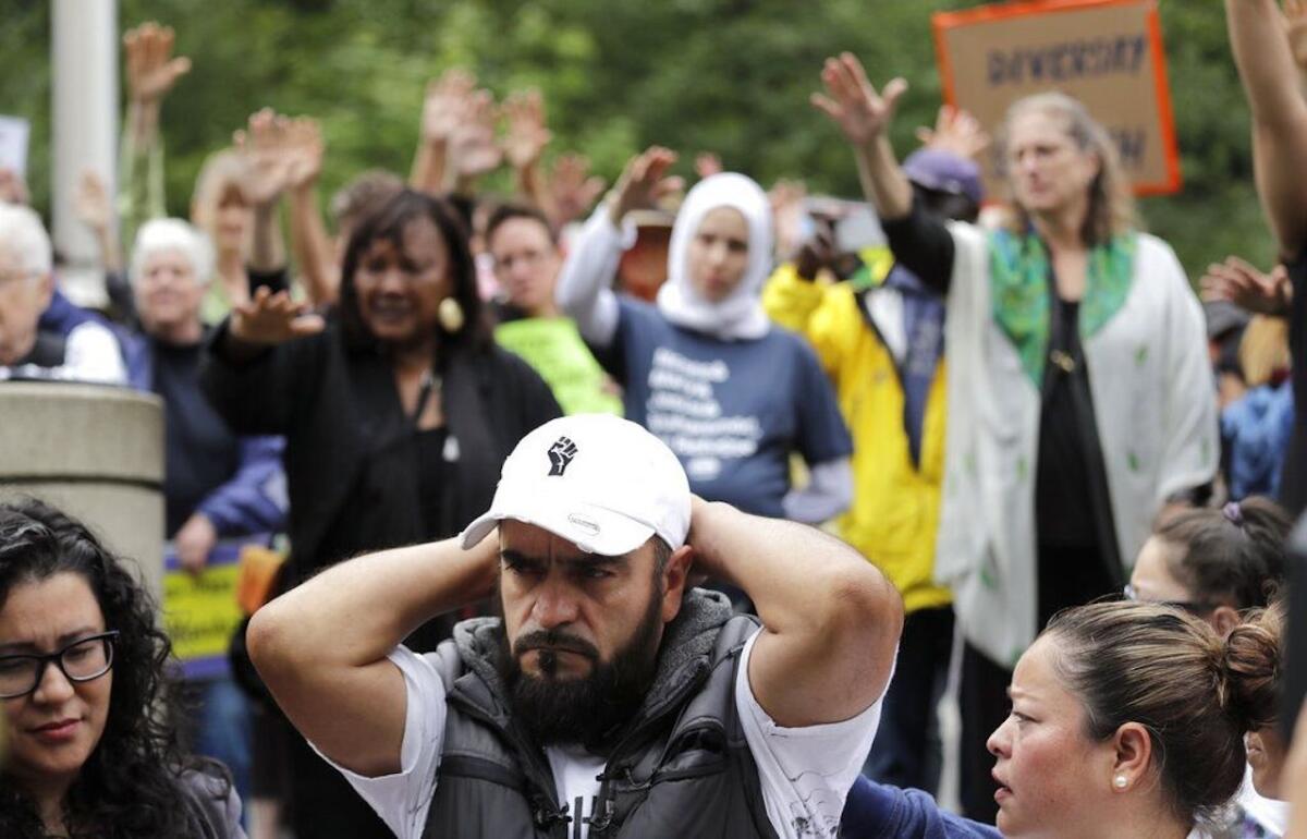 José Robles se lleva las manos a la nuca mientras simpatizantes extienden sus brazos en un tipo de bendición antes de que se presente ante autoridades del Servicio de Control de Inmigración y Aduanas en Tukwila, Washington, que lo arrestaron.
