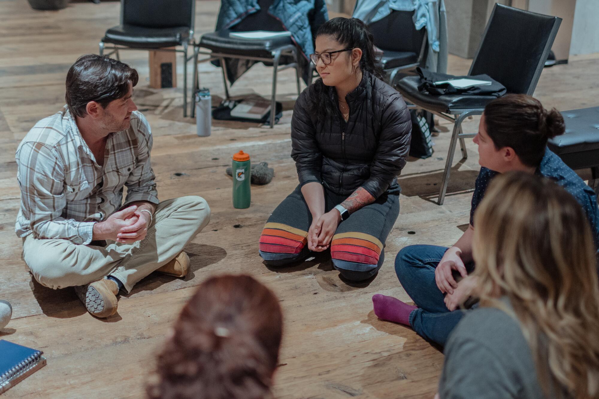 A few people sit in a circle on the floor talking 