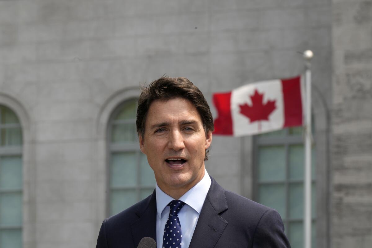 Prime Minister Justin Trudeau speaks to media. The Canadian flag flies behind him.