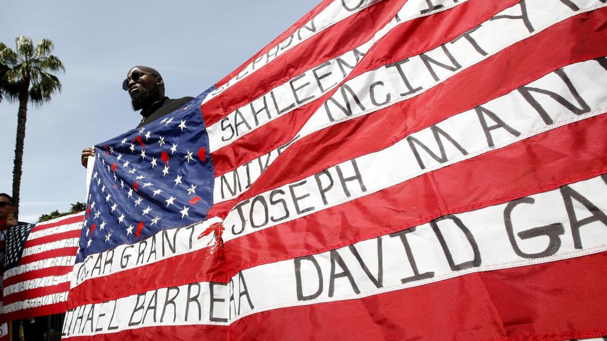Malaki Seku Amen holds up an American flag with the names of people shot and killed by law enforcement officers, as he joins others April 8 in Sacramento in support of a bill that would restrict the use of deadly force by police.