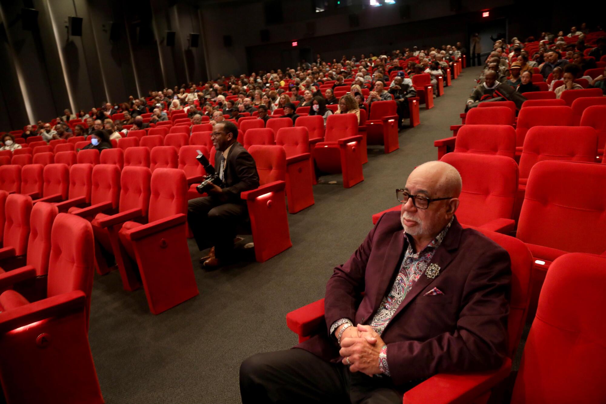 A man sits in a theater, away from other members of the audience.