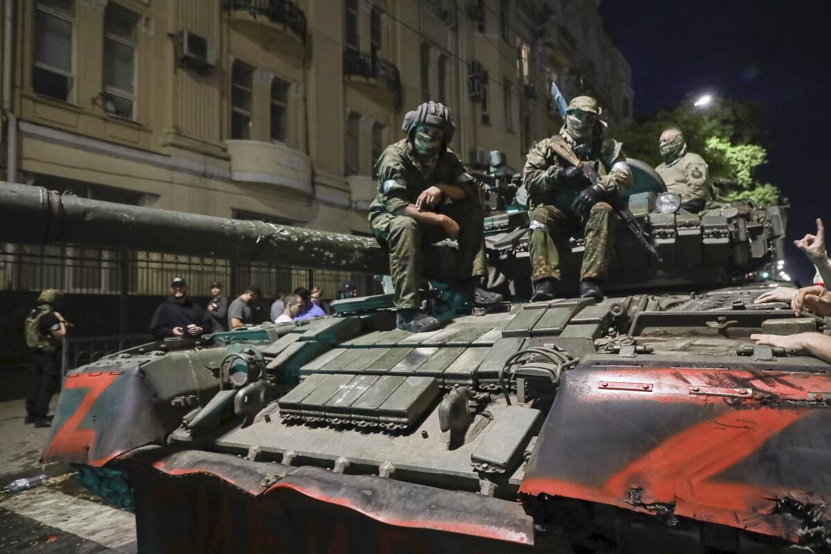Fighters in fatigues sit atop a tank on a city street