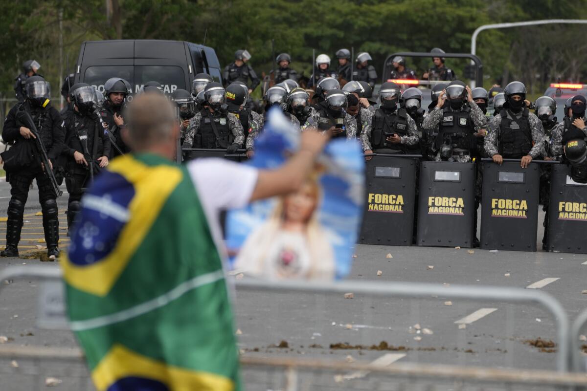 A supporter of Brazil's former far-right president Jair Bolsonaro is confronted by a phalanx of police in riot gear.