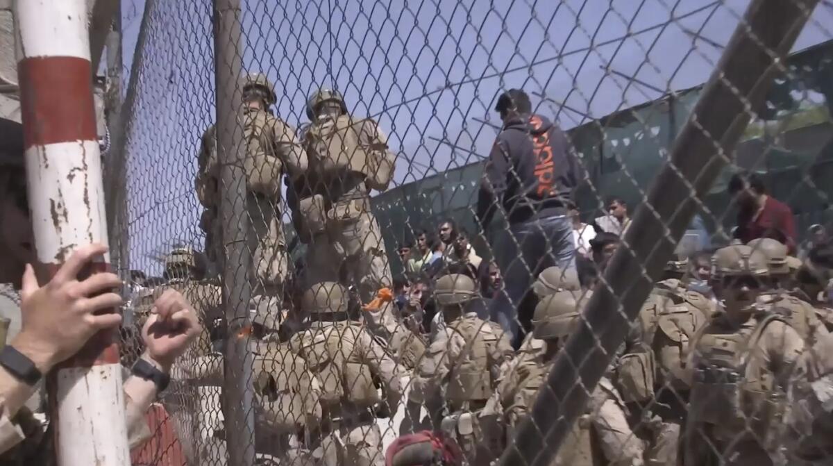 Troops in fatigues and hats are seen behind a chain-link fence 