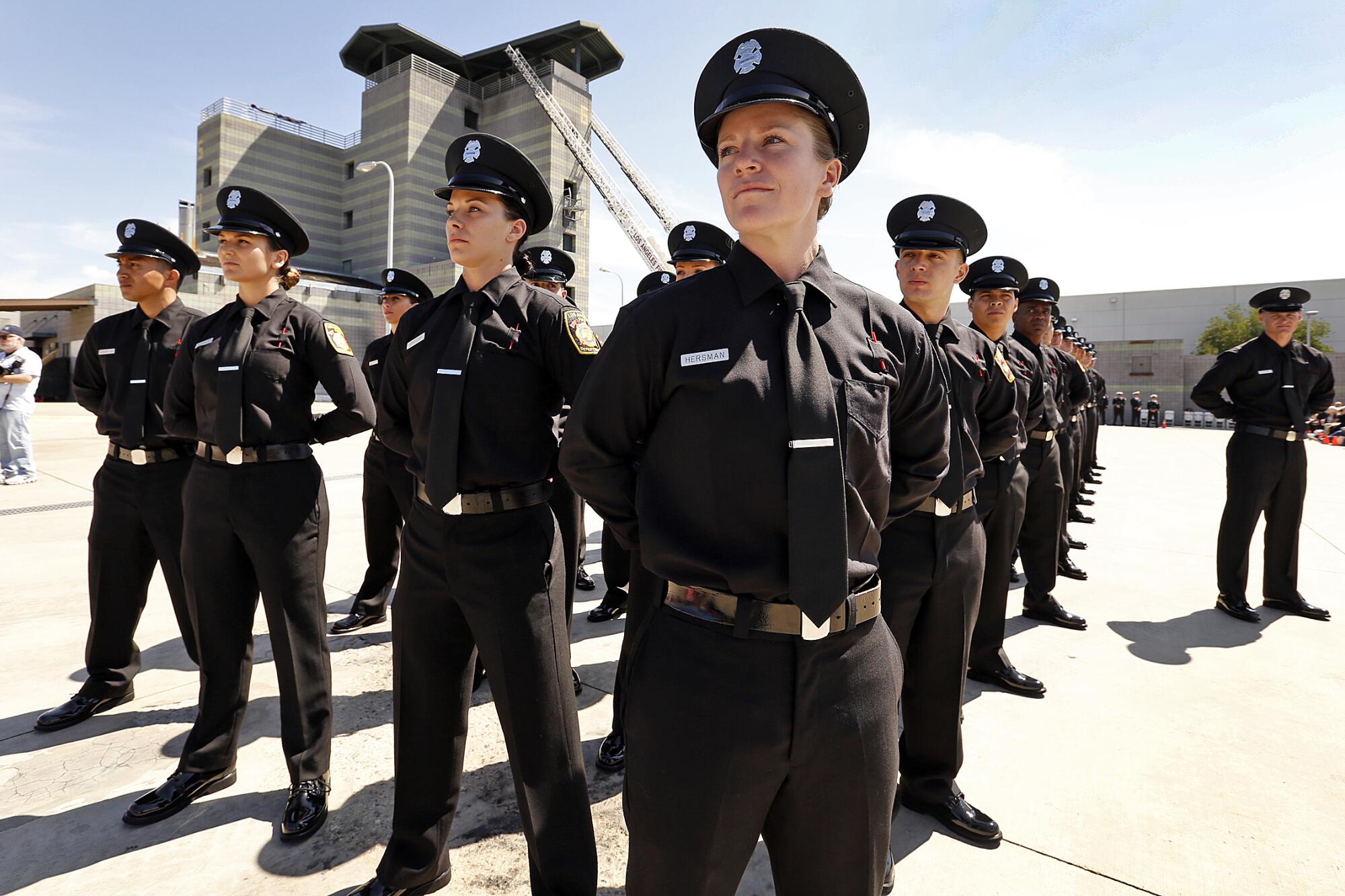 A group of graduating firefighter recruits stand in formation wearing black dress uniforms.