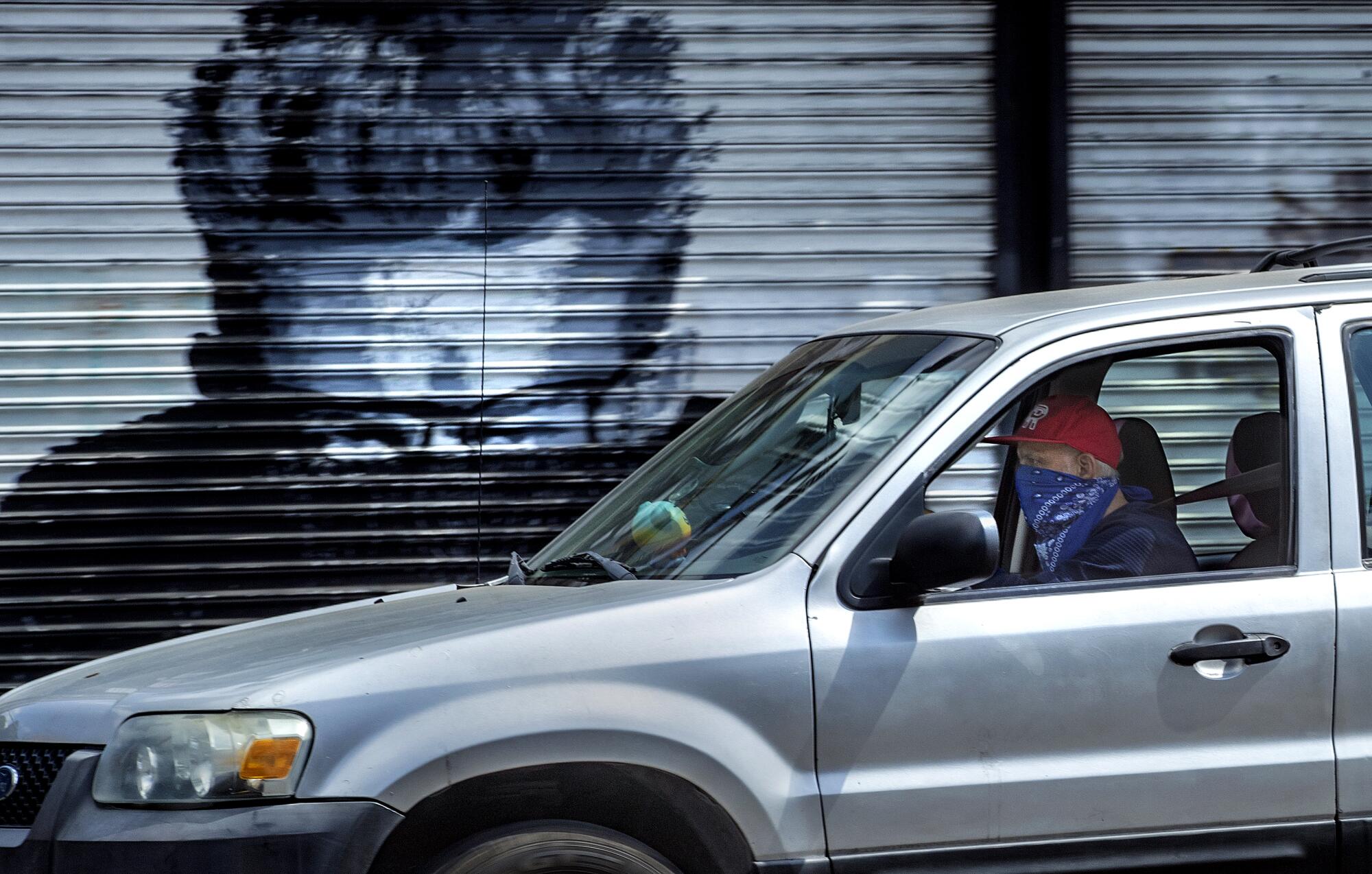 A masked motorist drives past a mural on Hollywood Boulevard in Hollywood.