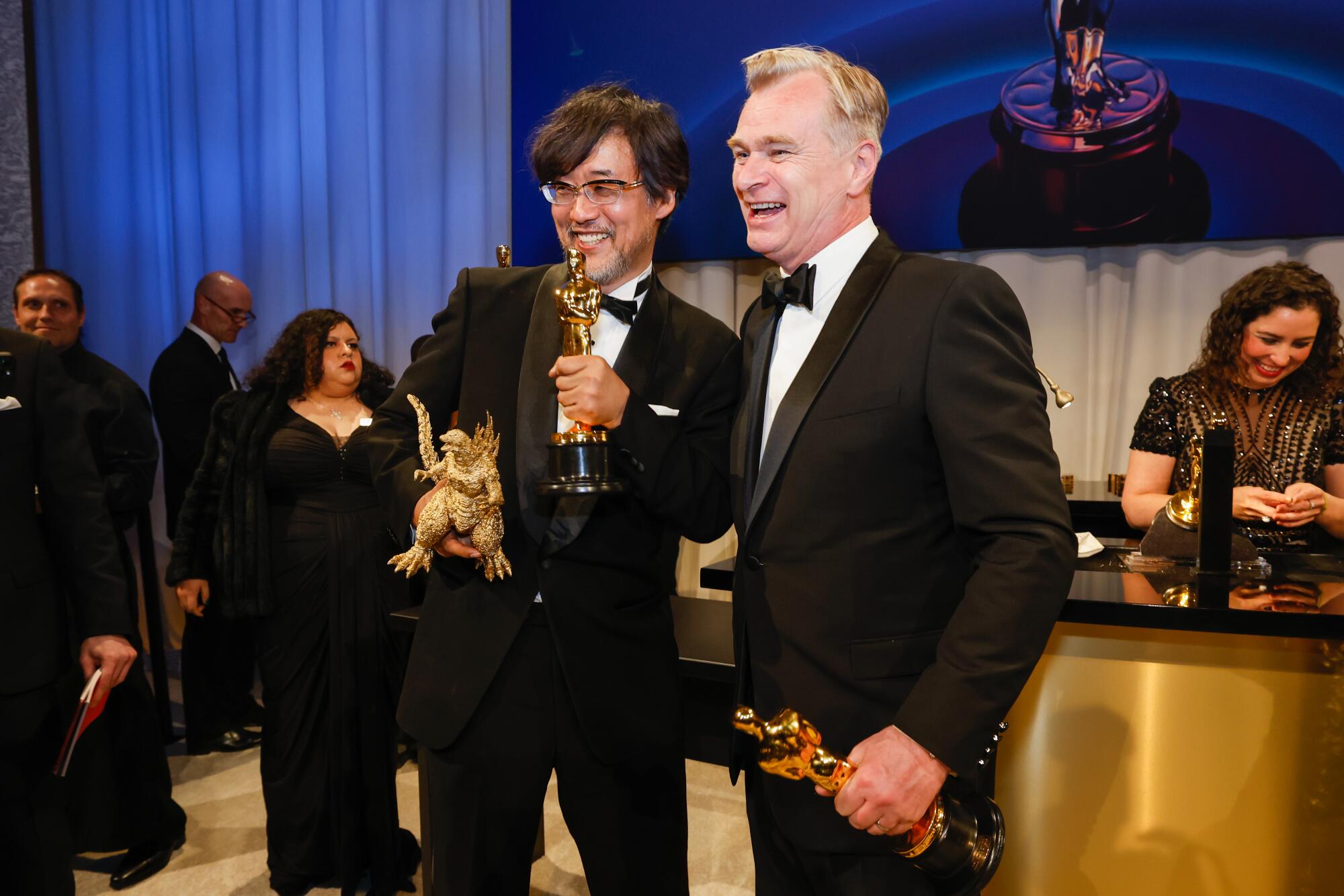 Two men hold their Oscars, one with a Godzilla statue in the other hand.