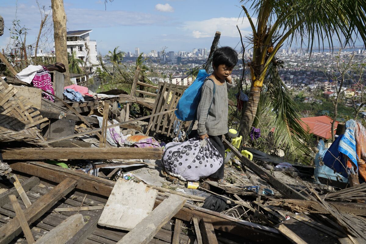 A boy walks amid a pile of lumber from a destroyed home carrying knapsacks