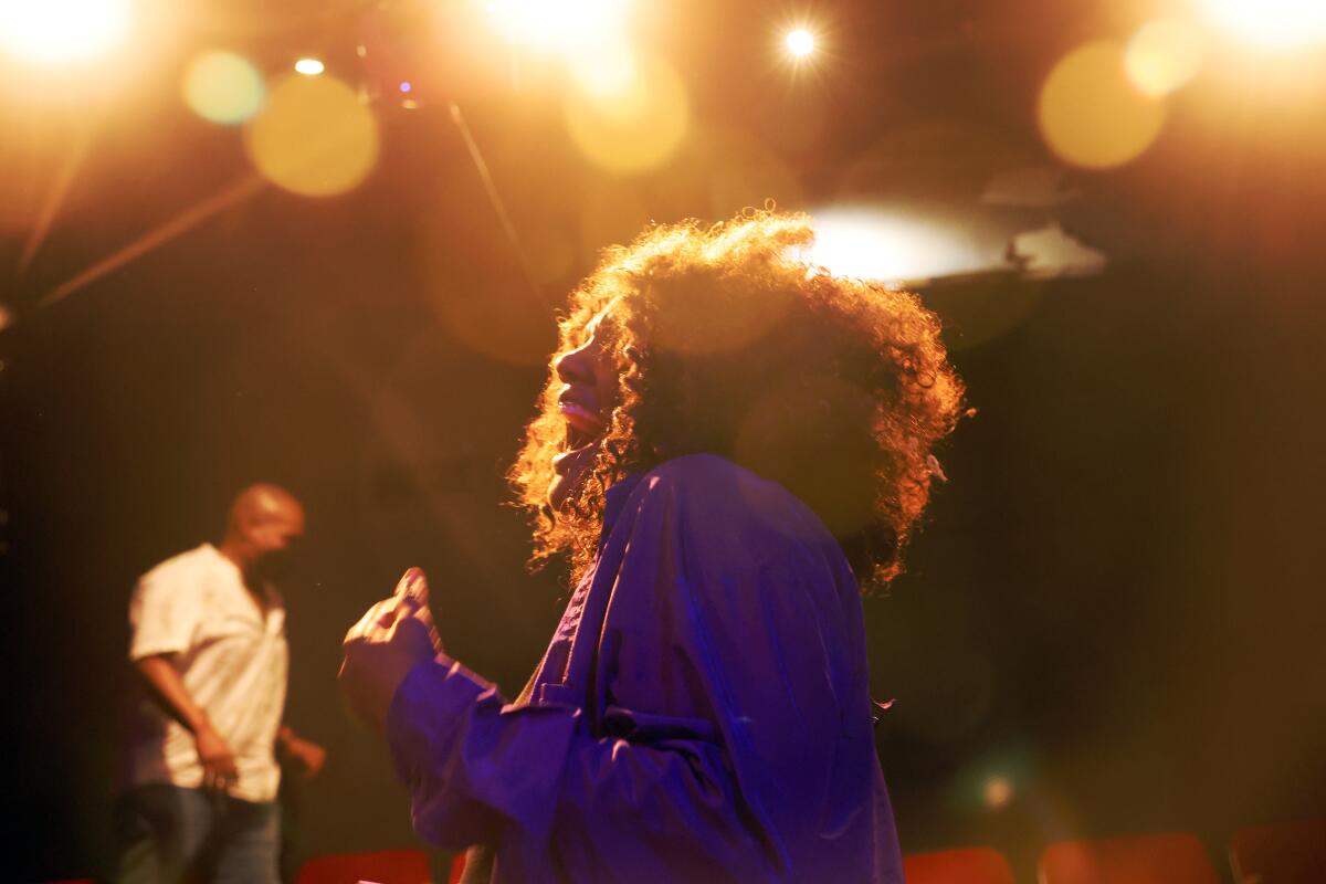 A woman in purple is seen laughing in profile, her curls illuminated by theater lights. A man is seen in the background.