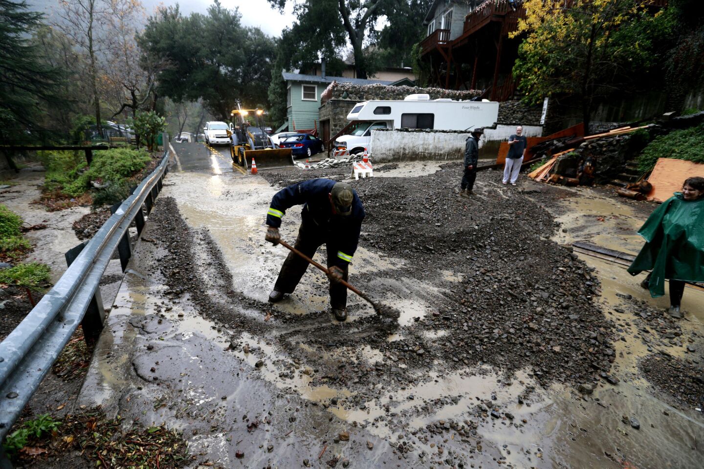 Crews remove mud flows across a road during a flash flood watch in the Silverado Canyon burn area.