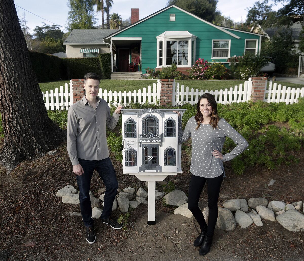 Luke and Jessica Cheney with a homemade puzzle trading post they made from a Barbie Grand Hotel and installed at Jessica's parents' Mountain Avenue home in La Crescenta.