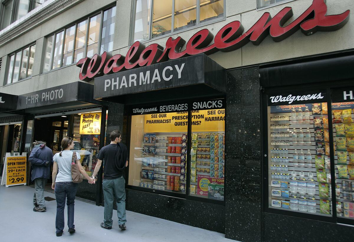 A couple holds hands on a sidewalk outside a Walgreens store.