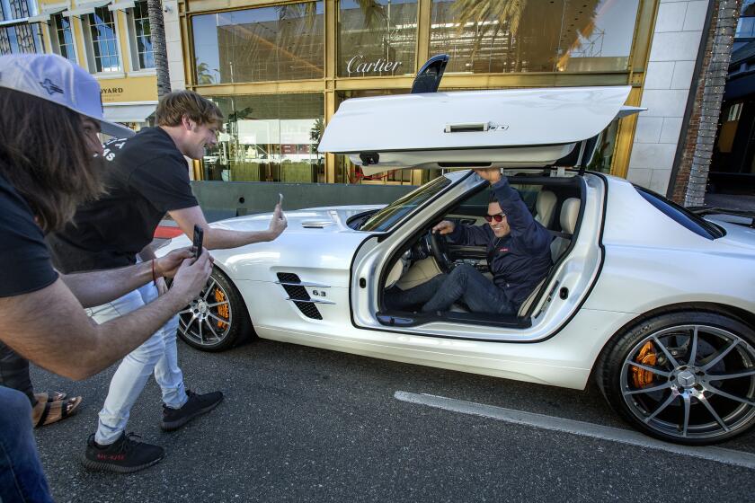BEVERLY HILLS, CA-NOVEMBER 16, 2022: Daniel MacDonald,25, 2nd from left, and his producer Blake Thompson, 25, use their iPhones to take video of a man stopped at a red light on Rodeo Drive in Beverly Hills as MacDonald asks the driver of the Mercedes SLS AMG car, "What do you do for a living?" The man answered that he is in the dental supply business. MacDonald's videos have gone viral and he has amassed millions of followers on TikTok, YouTube, and Instagram, becoming a millionaire himself in the process. (Mel Melcon / Los Angeles Times)