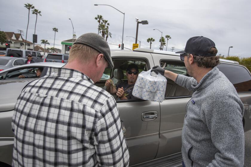 Troy Barton, left, and Mario Marovic hand a bundle of toilet paper to a customer in the parking lot of Malarky's Irish pub in Newport Beach on Friday, March 20. The bar sold thousands of rolls of toilet paper for $.50 (cents) each with a maximum of 10 rolls per customer.