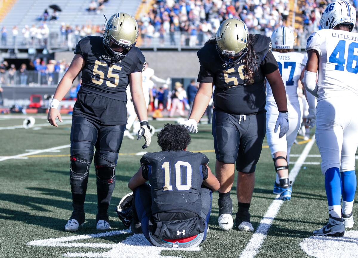 Birmingham quarterback Kingston Tisdell is helped off the field by two teammates.