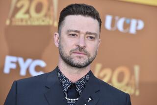 Justin Timberlake wears a printed shirt, black tie and blazer in front of an orange backdrop