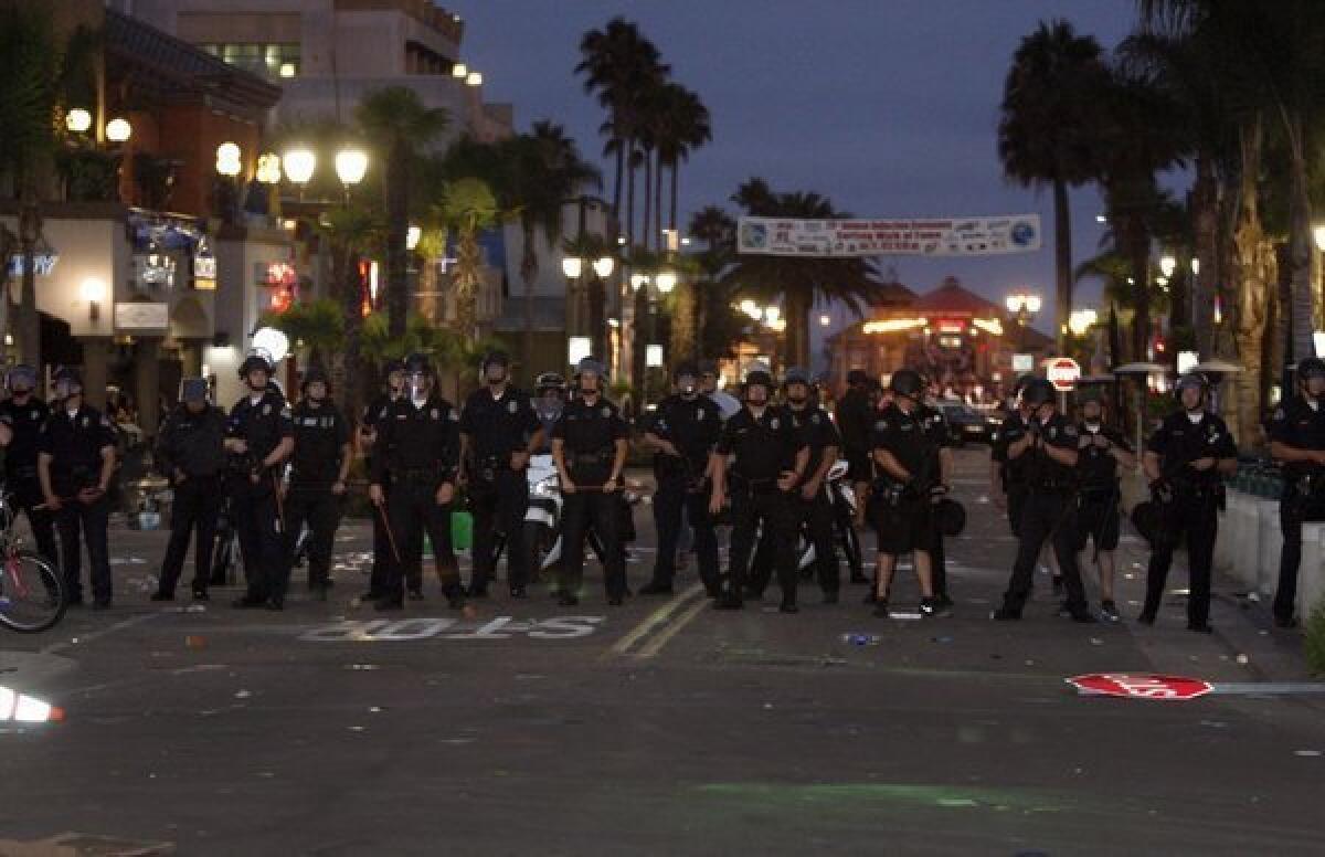 A large police presence moves rioters away from Main Street in Huntington Beach following a surfing contest on July 28.