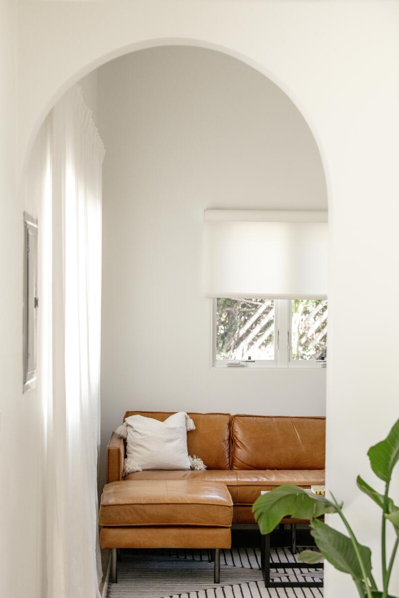A Spanish-style white arched doorway with a view into a living room with a brown leather couch