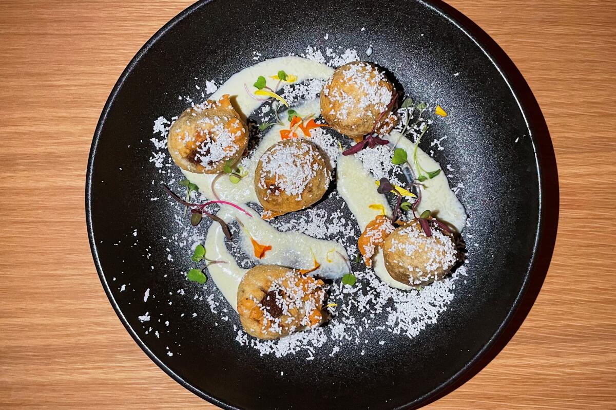 An overhead photo of five mushroom and gruyère beignets on a black plate.