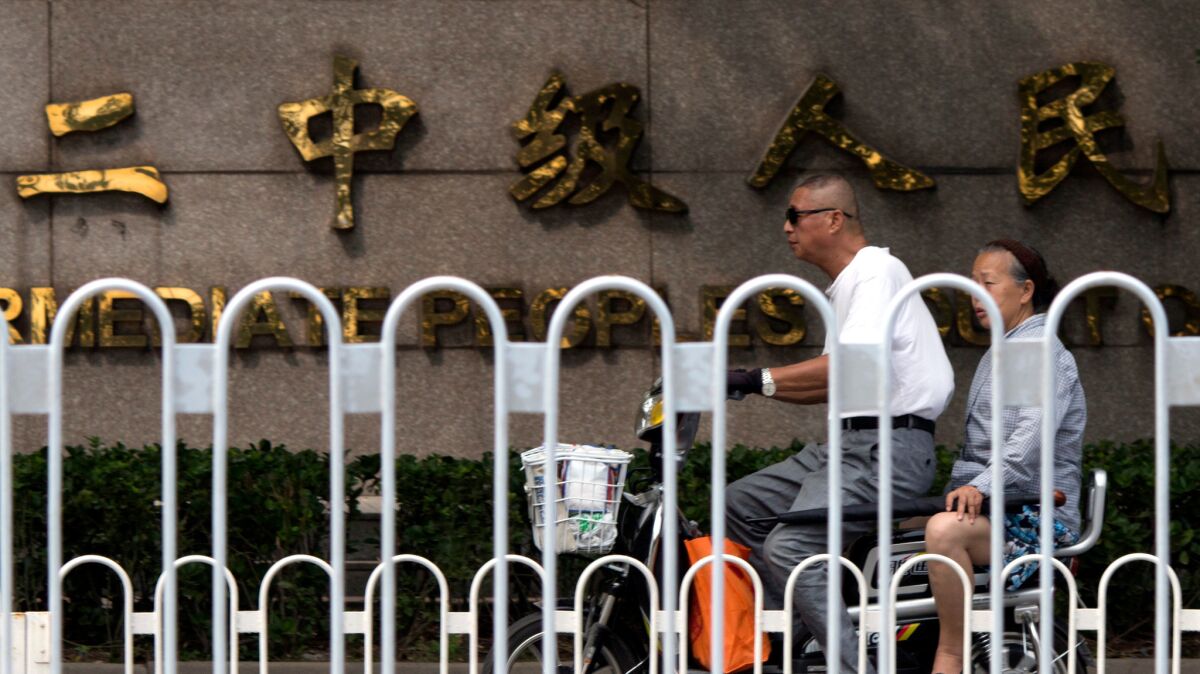 An elderly man and woman ride on an electric bike past a sign for Tianjin No. 2 Intermediate People's Court, where Hu Shigen, a writer and member of underground Christian churches, was tried.
