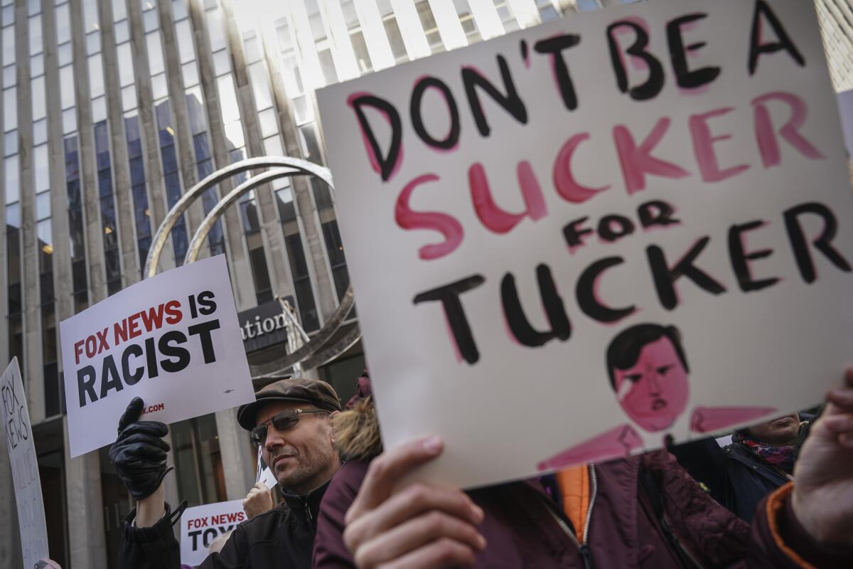 Protesters rally against Fox News outside the News Corp. building with signs.