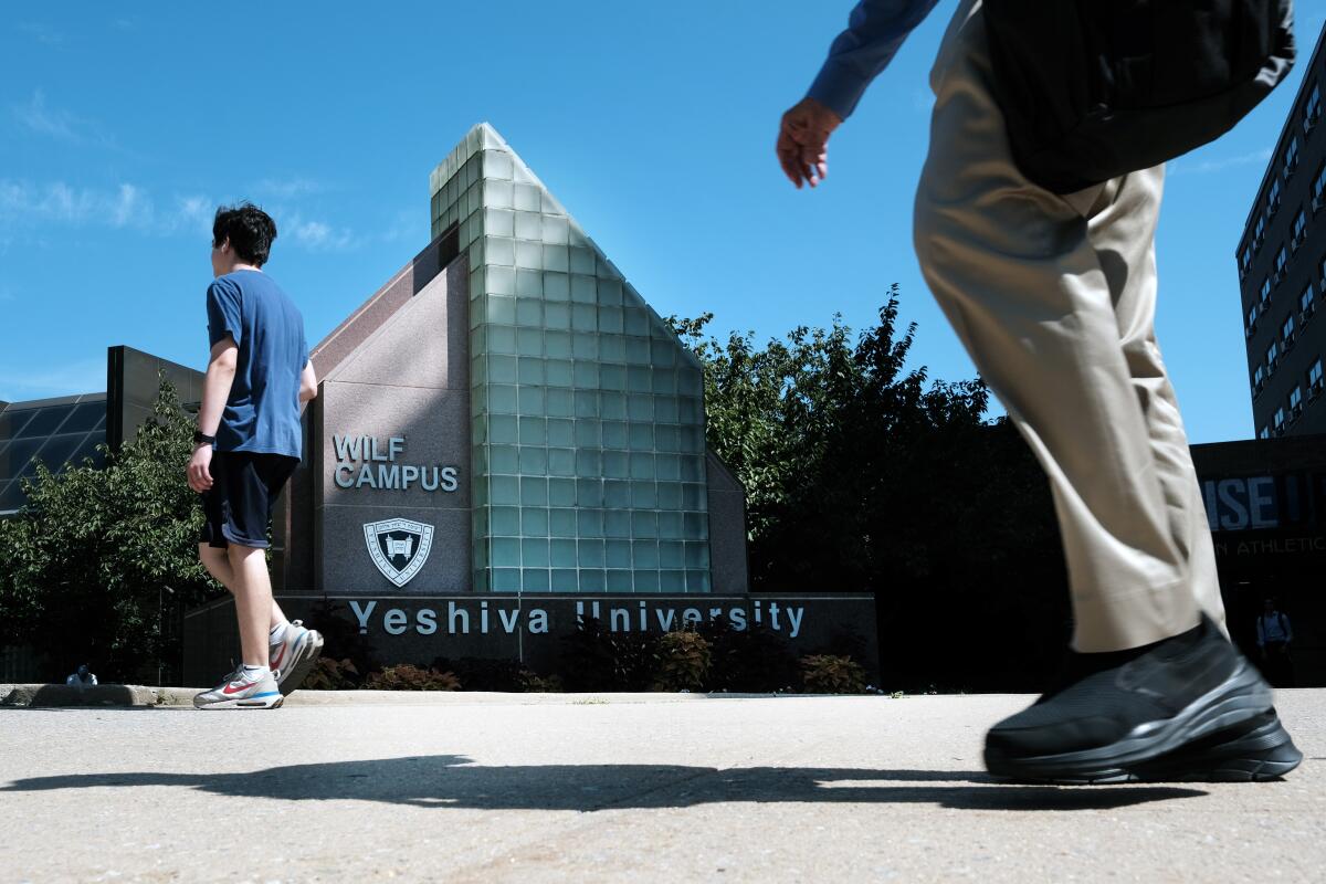 A student in shorts and a T-shirt walks on Yeshiva University's campus; photo includes a closeup of another student's legs  