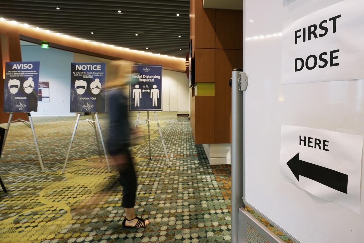 A woman walks toward a sign that says "First Dose Here."