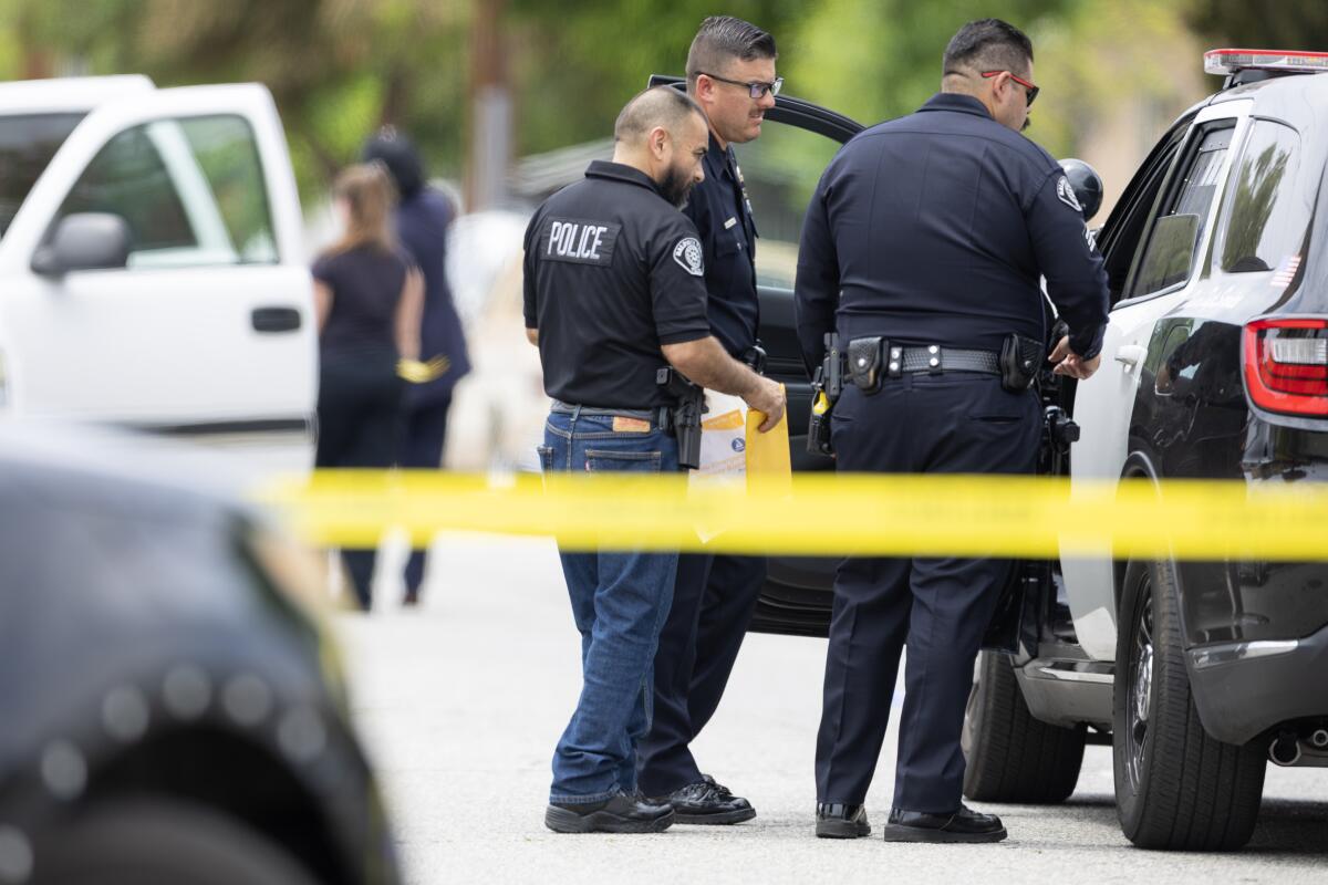 Law enforcement officers stand behind police tape.