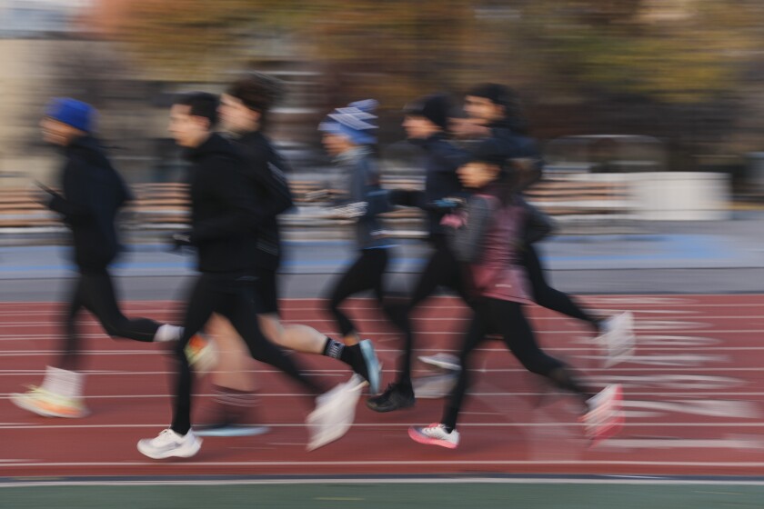 A group of adult runners dressed for cool weather head around a track.