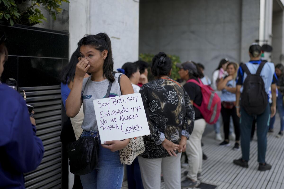 Una mujer sostiene un cartel mientras hace fila con otras personas afuera de la oficina 