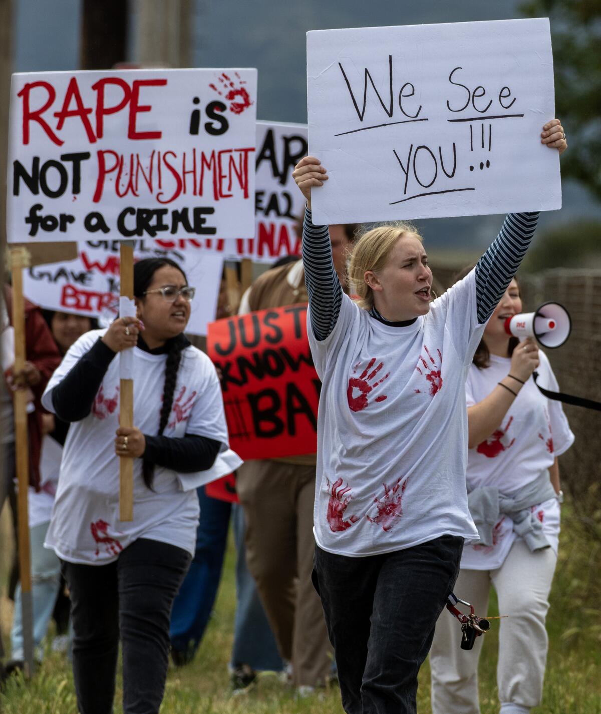 Protesters hold signs during an outdoor march.