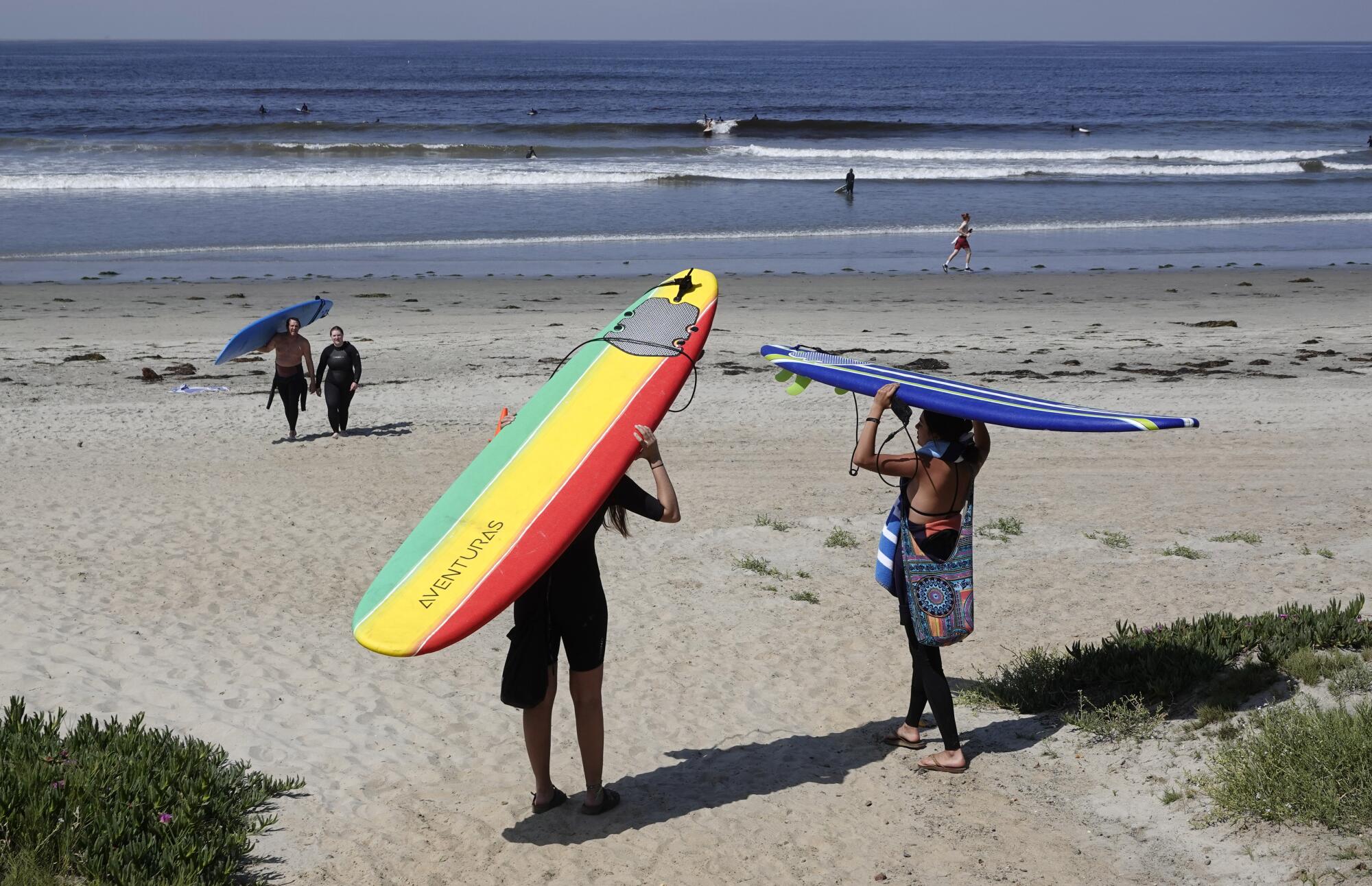 Andrea Lizardi, left, and Angeli Ruvalcaba walk to surf in Pacific Beach after local beaches reopened to activities such as walking, running, and surfing on April 27, 2020. Beaches have been closed for several weeks due to the coronavirus.