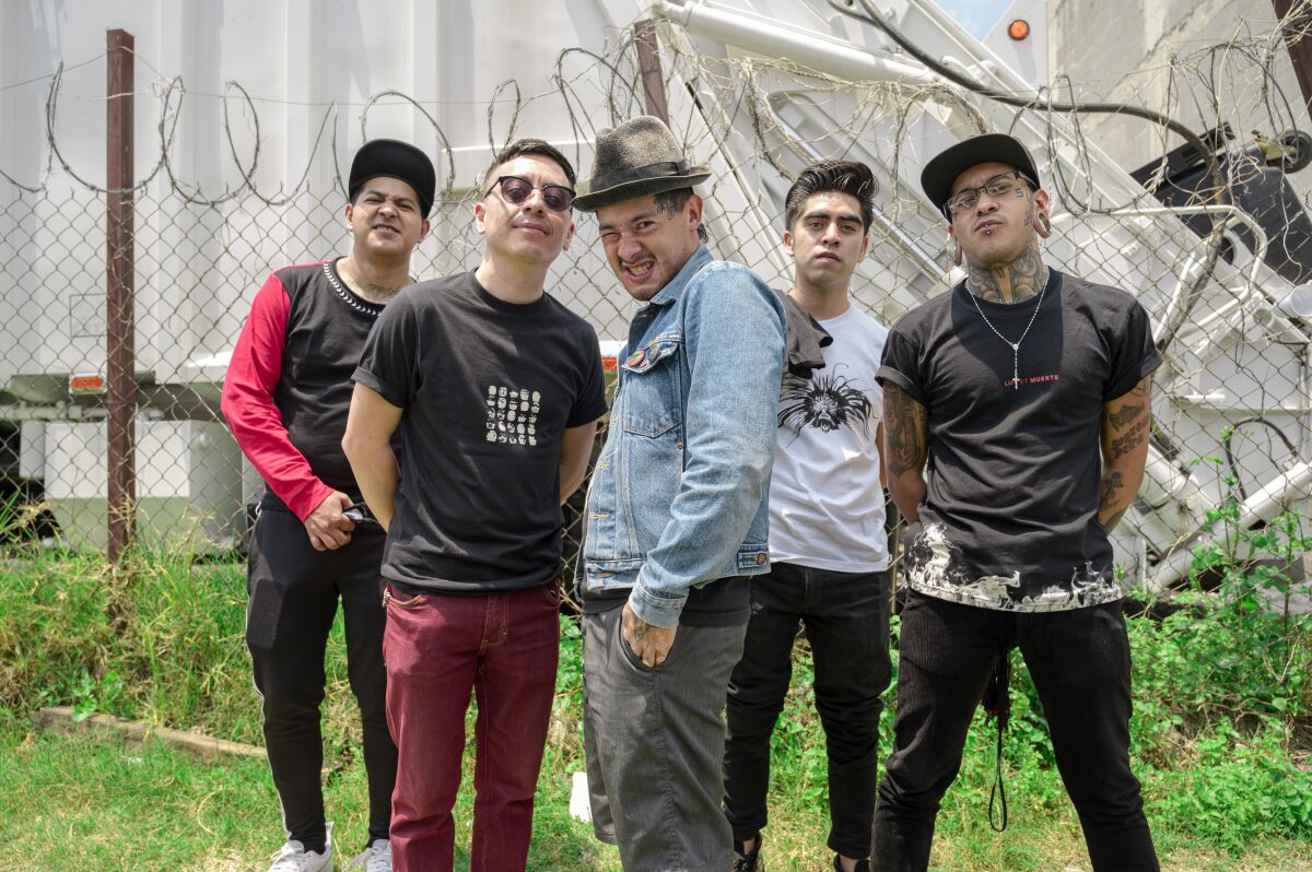 A group of five punk men pose by a fence with barbed wire 