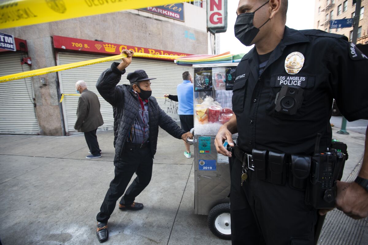 A vendor moves his pushcart as an LAPD officer clears the corner of South Broadway and 7th Street of pedestrians.