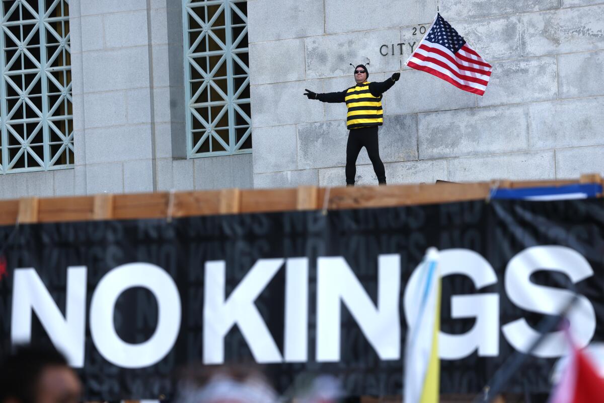 A man dressed as a bee holds an American flag at a No Kings protest.