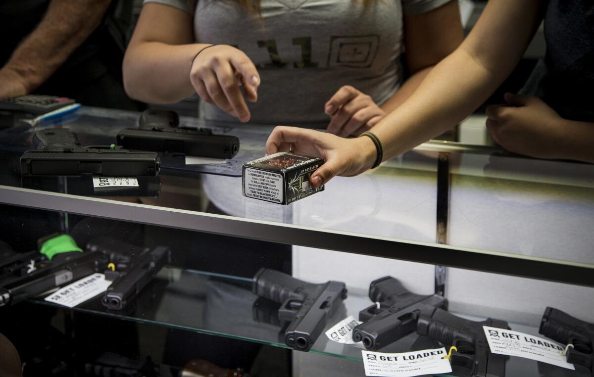 A box of firearm ammunition is held at a counter at a store in Grand Terrace, Calif., in 2016. Handguns are also shown.