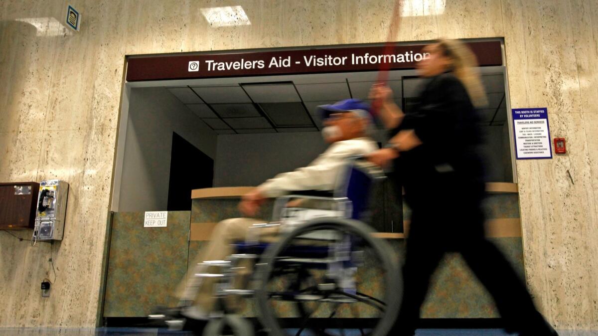 A traveler in a wheelchair is pushed past an information desk in Terminal 1 at LAX.