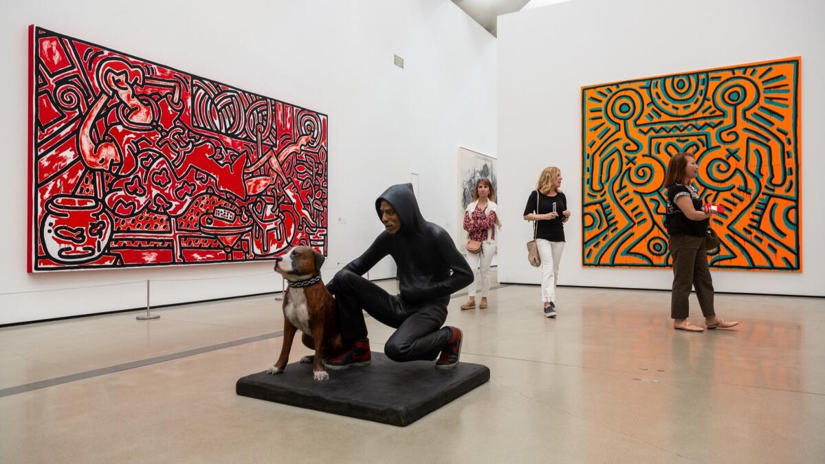 People walk through the gallery, in view of Keith Hering's "Red Room," on the left, and "Untitled," on the right, and John Ahearn's "Raymond and Toby," in the center.