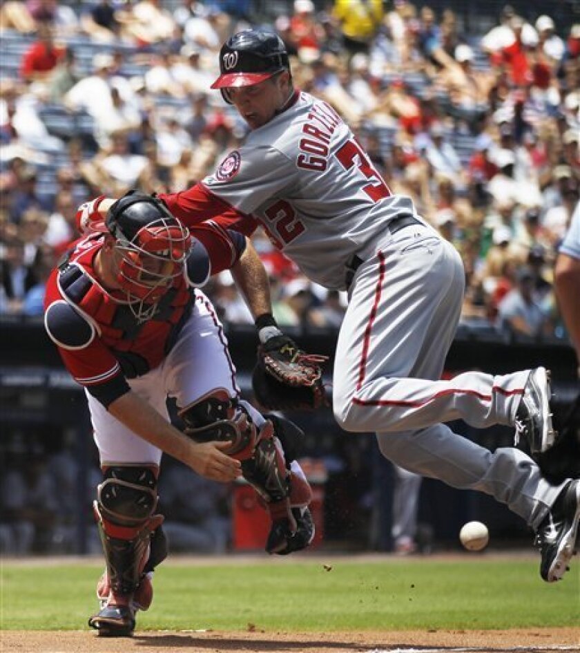 Washington Nationals' Tom Gorzelanny (32) scores on a Roger Bernadina two-run triple as Atlanta Braves catcher Brian McCann (16) looks for the late throw in the third inning of a baseball game in Atlanta on Sunday, July 17, 2011. (AP Photo/John Bazemore)