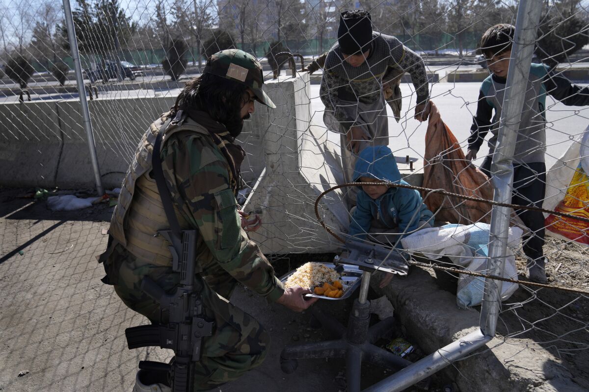 A Taliban fighter gives his meal to boys outside the Interior Ministry, in Kabul, Afghanistan, Thursday, Feb. 10, 2022. (AP Photo/Hussein Malla)
