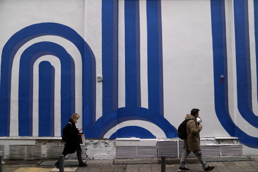 Unas personas caminan frente al mural "Olas" del artista Adioshpe en Atenas, Grecia, el miércoles 12 de enero de 2022. (Foto AP/Thanassis Stavrakis)