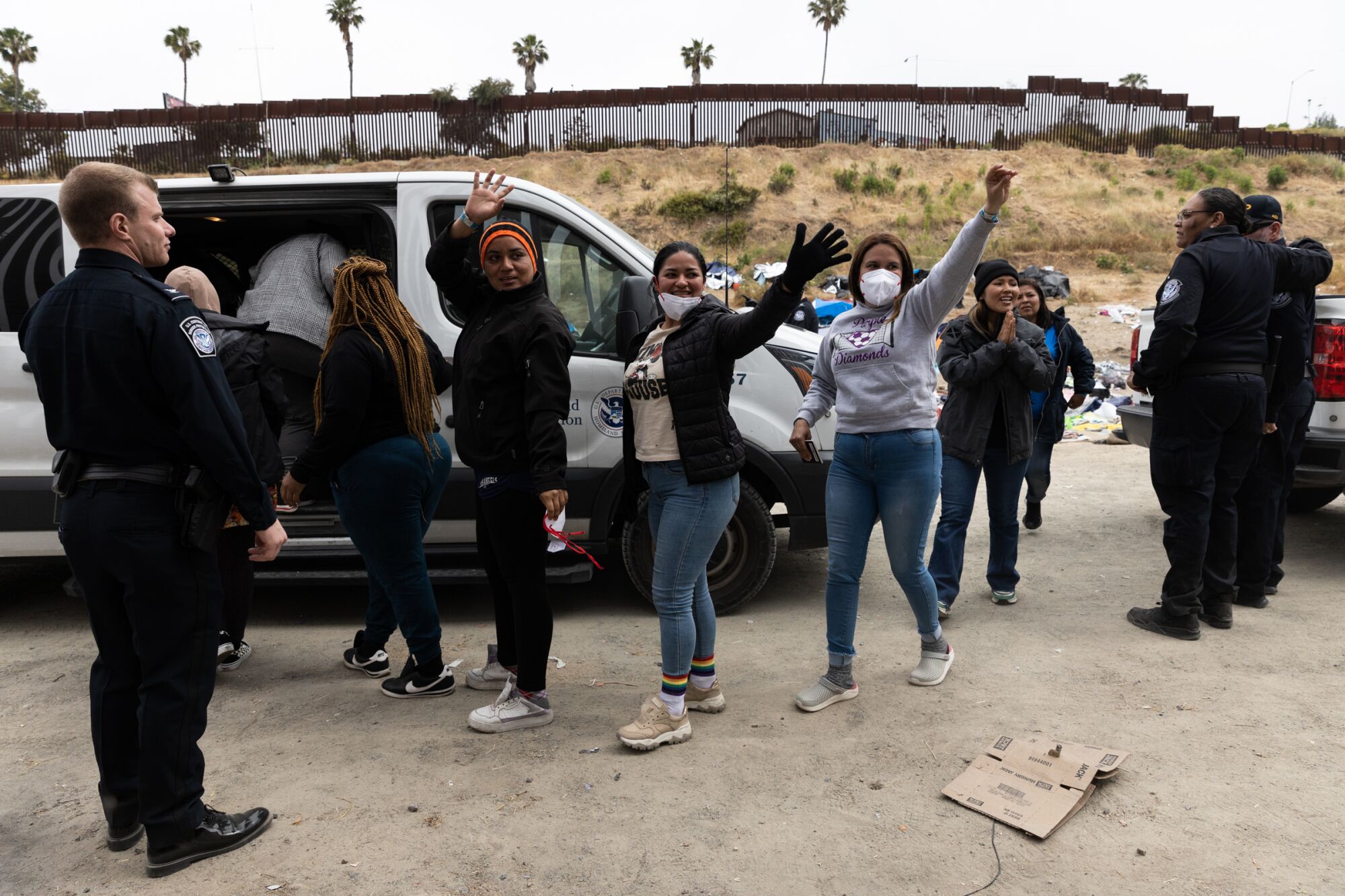Migrants wave to volunteers as they go into a van to be taken to processing centers at the U.S.-Mexico border 
